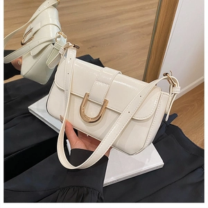Close-up of cream glossy patent leather shoulder bag featuring a golden U-shaped clasp