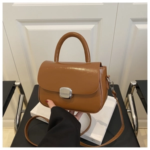 Detailed view of brown glossy leather bag featuring silver metal buckle and top handle
