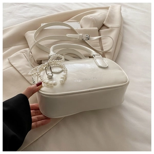 Détail du sac polochon beige minimaliste avec chaîne perlée et lettrage sur le cuir