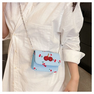 Light blue crossbody bag with cherry patterns and diamond buckle worn on white shirt