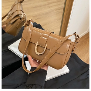 Detailed close-up of brown patent leather bag featuring a gold U-shaped metal buckle