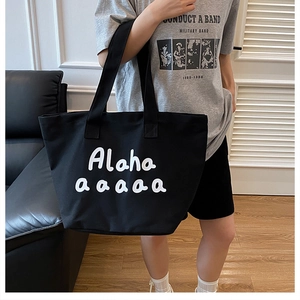 Close-up of black canvas tote bag with white bold lettering and wide shoulder straps