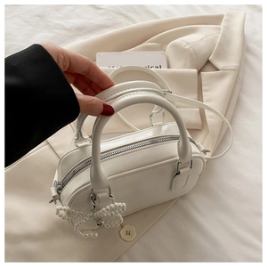 Détail du sac polochon blanc avec pendentif nœud en perles et fermeture zippée argentée