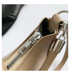 Detailed close-up of smooth silver zipper and decorative padlock charm on beige leather bag