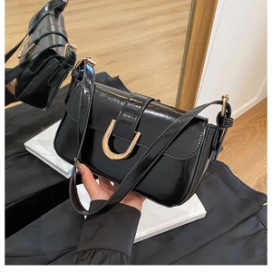Detailed close-up of a black glossy shoulder bag with a gold horseshoe buckle accent