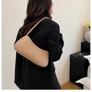Detail of minimalist beige underarm bag with gold bow clasp worn by a model