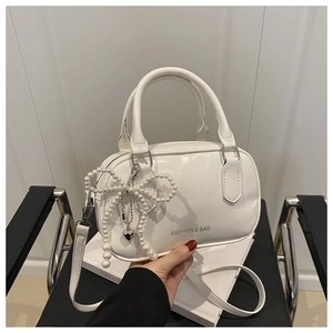 Détail du sac polochon blanc brillant avec nœud en perles et pendentif cœur élégant