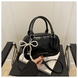 Gros plan sur un sac polochon en cuir verni noir avec pendentif nœud en perles et logo