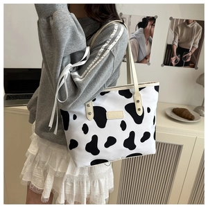 Close-up of a cow print tote bag with cream handles and a rectangular logo patch