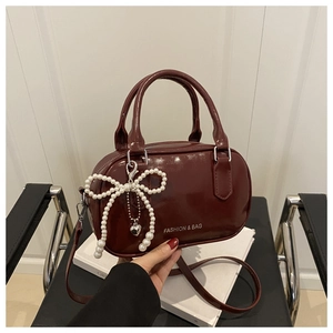 Détail du sac en cuir verni bordeaux avec breloque nœud perlé et poignée haute