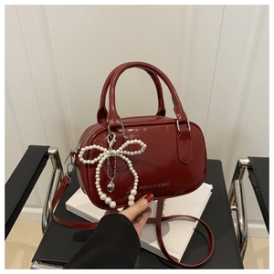 Détail du sac oreiller en cuir verni bordeaux avec nœud perlé et logo argenté