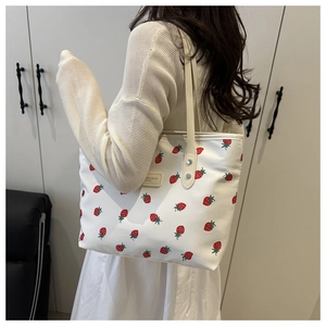 Detailed back view of a white tote bag with red strawberry prints worn under the arm