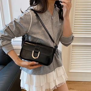 Glossy black underarm bag with gold metal buckle shown on model in urban casual outfit