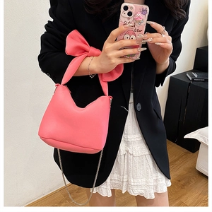 Detailed view of pink bow bucket bag with silver metal chain on a black and white outfit