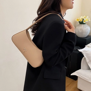 Chic beige leather underarm bag with a silver bow detail worn by a model in a blazer