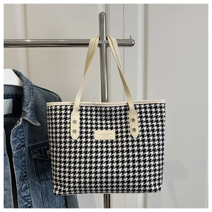 Detail of houndstooth tote bag featuring reinforced cream handles and leather logo patch