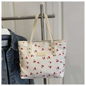 Detail of canvas tote bag with red cherry print and logo patch on white background