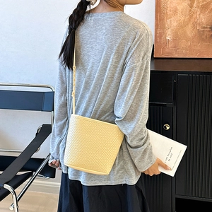 Minimalist light yellow woven bucket bag for women with cross-body strap and texture