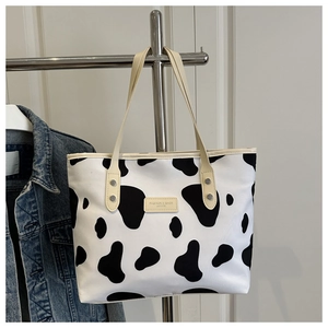 Detail of cow print canvas tote bag featuring leather label and reinforced handles