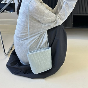Minimalist light blue woven leather bucket bag shown in a stylish lifestyle setting