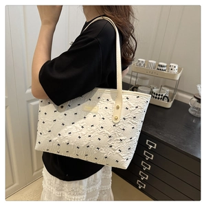 Detail of a beige tote bag with black bow patterns and elegant texture on a model shoulder