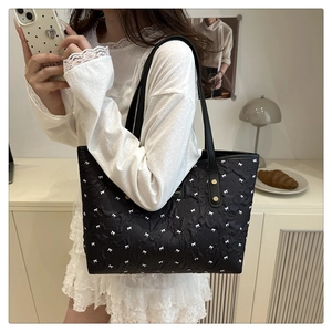 Detail of black tote bag featuring white bow jacquard pattern and leather handles