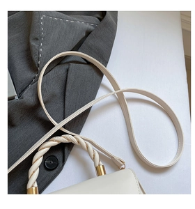 Detail of minimalist cream leather handbag featuring twisted knot handle and gold hardware
