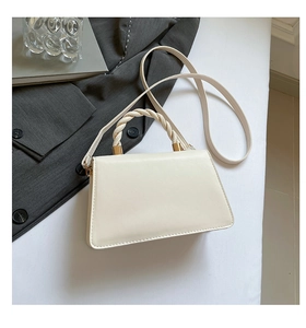 Detail of cream crossbody bag featuring a twisted handle and gold hardware accents
