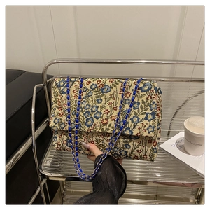 Close-up of floral tapestry envelope bag with blue woven metal chain and woven fabric detail