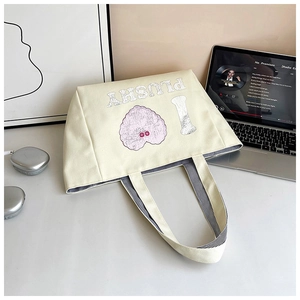 Detail of canvas tote bag showing pink heart graphic and striped handles on a desk