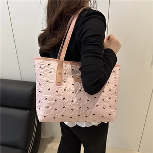 Pink pleated tote bag with black bow patterns and leather handles for casual commute