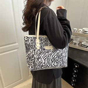 Fashionable zebra print tote bag with beige handles worn by a model in a minimalist setting