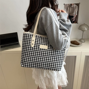 Large houndstooth tote bag with cream leather handles and silver studs shown on a model
