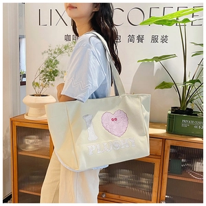 Close-up of a large beige canvas tote bag with pink heart plushy graffiti on a model