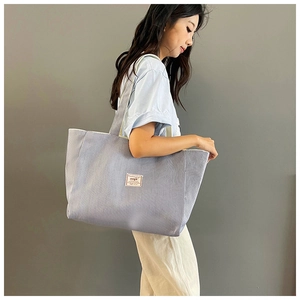 Side view of large light blue corduroy tote bag worn by a model against a grey wall