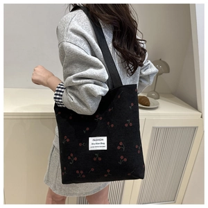 Detail of black corduroy tote bag with red cherry prints and white square label