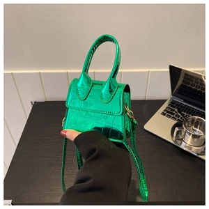 Detail view of mini green crocodile pattern handbag with glossy finish and top handle