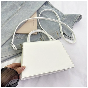 Detail of a white trapezoid handbag with silver hardware on denim and white background