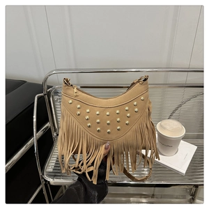 Detailed view of beige suede crescent bag with golden rivets and long fringe tassels