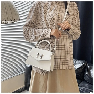 Detailed view of white crossbody bag with silver bow buckle and adjustable strap worn by model
