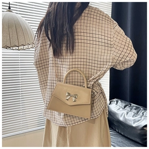 Beige crossbody bag with gold bow buckle shown on model in a daily scene setting