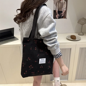 Black corduroy tote bag featuring red cherry prints and woven shoulder straps
