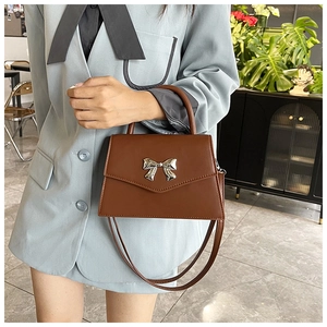 Close-up of a brown matte faux leather handbag with a silver metal bow buckle detail