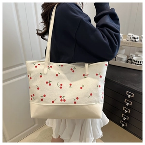 Gros plan d'un sac cabas blanc avec motifs cerises porté par une personne