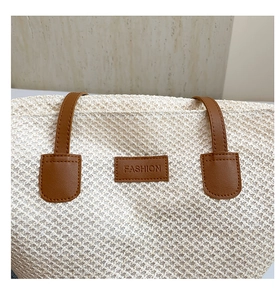 Détail d'un sac en paille tressée avec écusson en cuir marron et texture des poignées