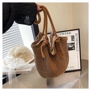 Detail of brown woven straw tote bag with rope handles and tassel accent for summer
