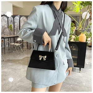 Detail of black mini crossbody bag with metal bow decoration on light blue blazer