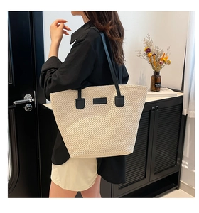 Gros plan du sac cabas en paille crème avec texture tissée et bandoulière noire contrastée