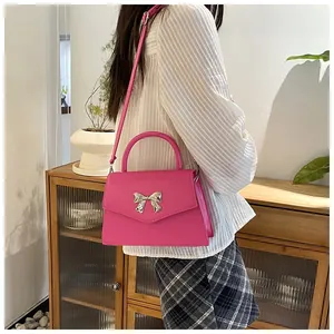 Pink handbag with metal bow detail and crossbody strap shown in a lifestyle setting