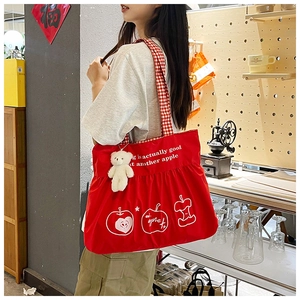 Detail of red canvas tote with white apple print, checkered strap and plush bear charm